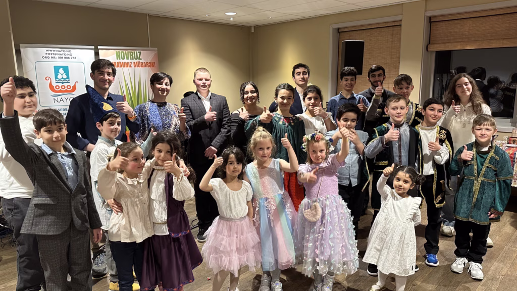 Masse barn som viser tommel opp til kamera, foran plakater der det står NAYO og Novruz.