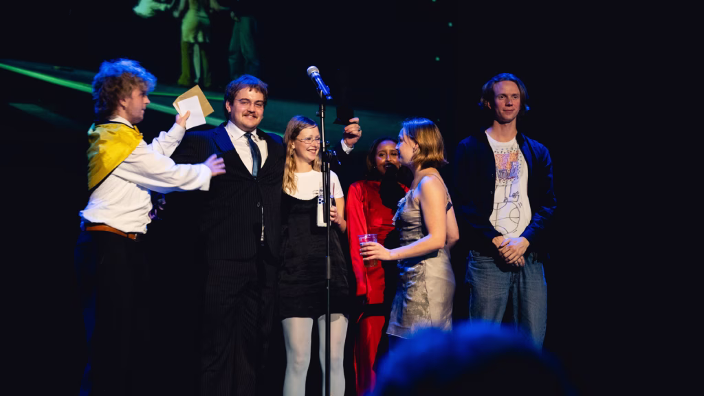 6 unge mennesker står på en scene med en mikrofon